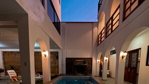 A swimming pool with a stone surround, a stone fireplace, and a covered seating area with lounge chairs. - Gamora Hotel Playa (Los Organos)