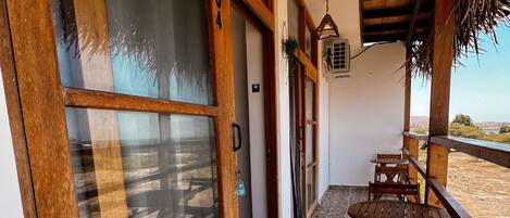 A wooden-framed door with a frosted glass panel, a stone-tiled floor, and wooden tables and chairs on a balcony with a view.