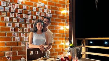 Una pareja cenando en una mesa con una pared de ladrillo decorada con fotografías, una botella de champán y un balde con hielo.