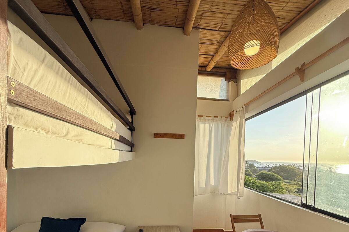 Una camera con un letto a castello, un comodino in legno, un tavolo con sedie e una vista attraverso ampie finestre.
