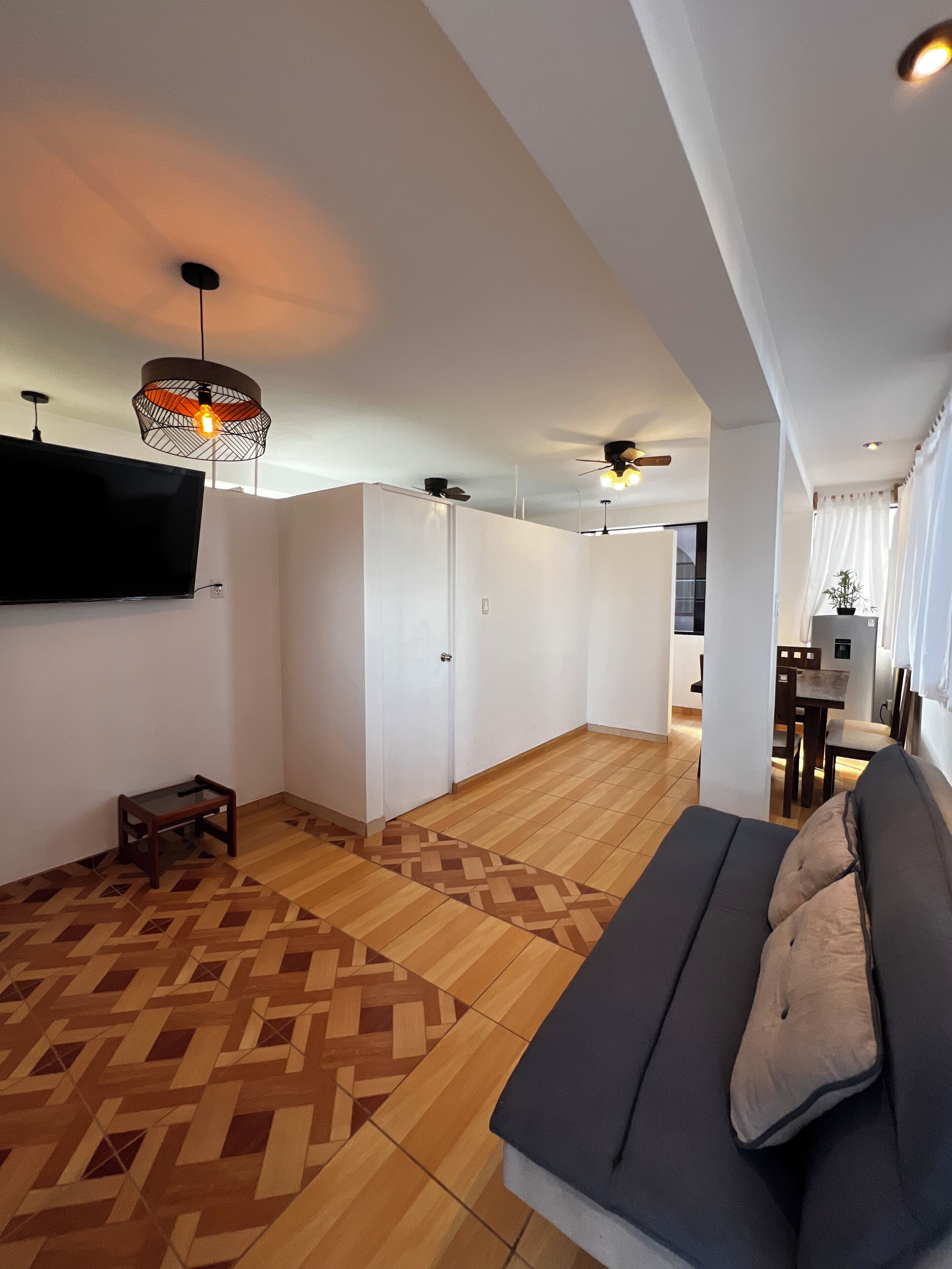 A modern living room with a sofa, a TV mounted on the wall, and a patterned wooden floor.