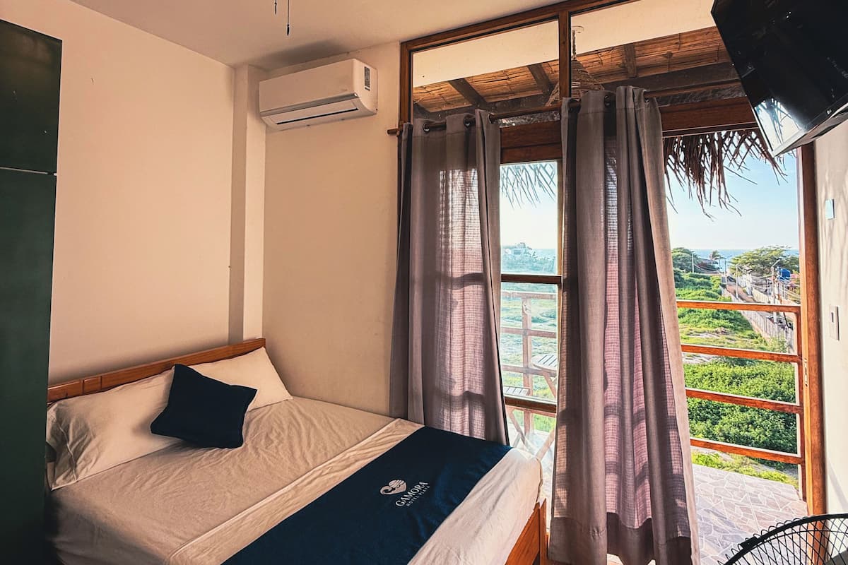 Camera da letto con un letto, una ventola a soffitto, un condizionatore d'aria, una TV e vista sul verde dalla finestra.
