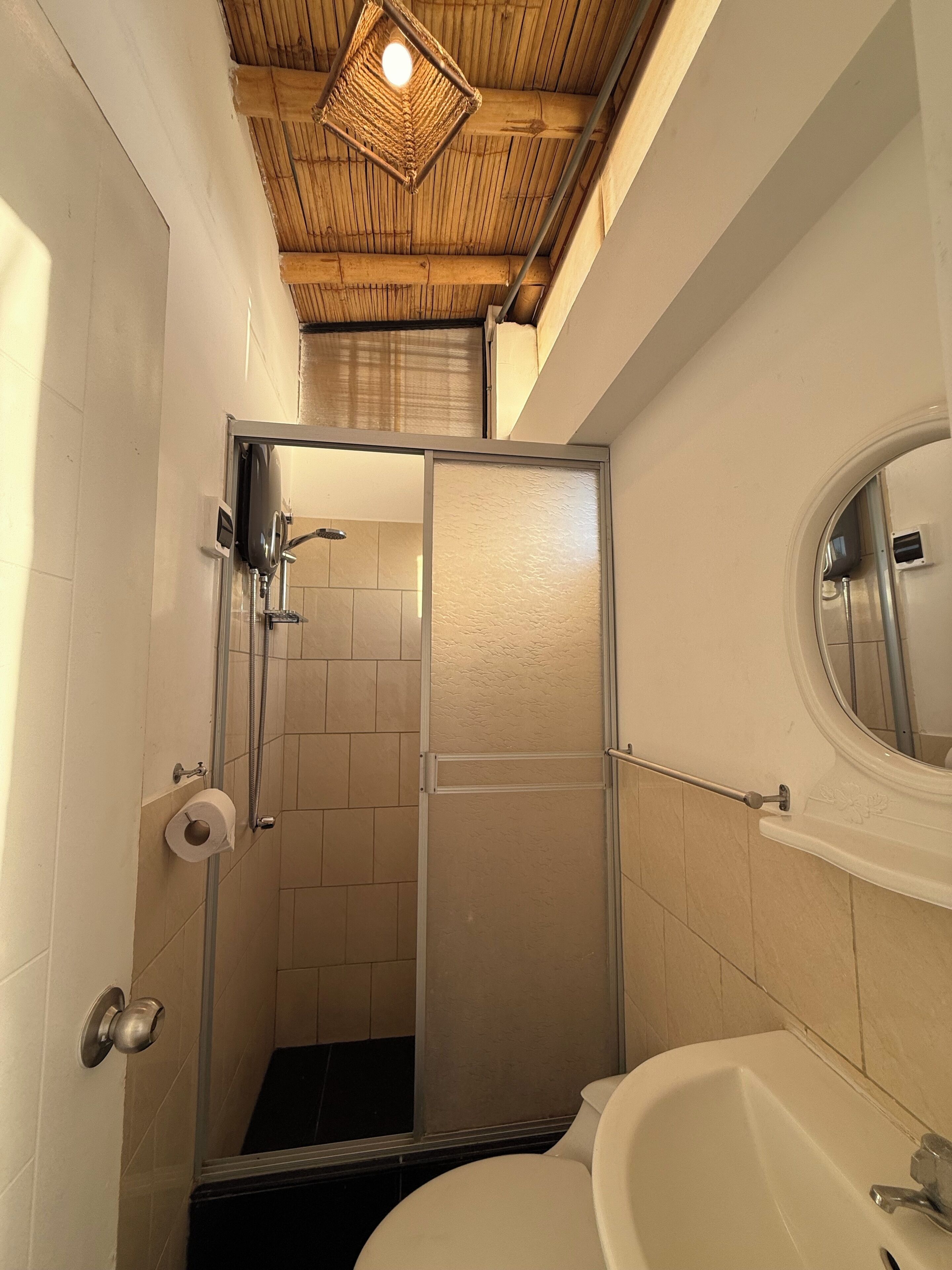 A bathroom with a shower, toilet, and sink, featuring a wooden ceiling and tiled walls.