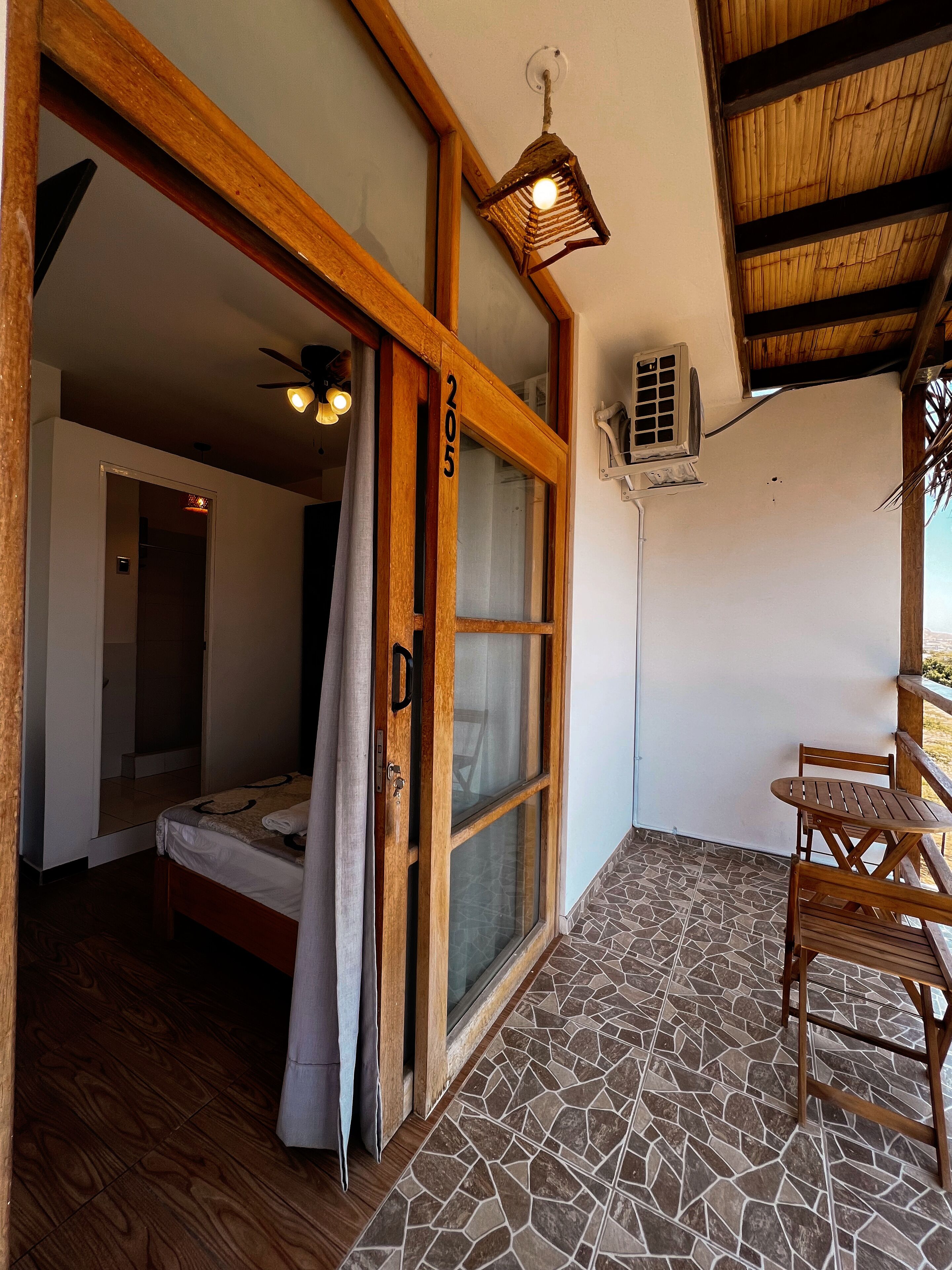A room with a bed, a wooden door, a window, a ceiling fan, and a small table with chairs.