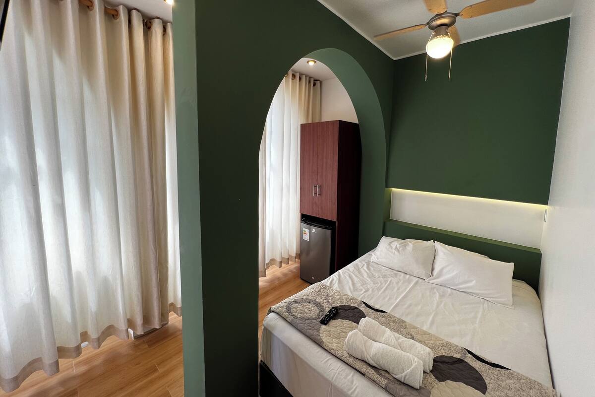 Una camera d'albergo con un letto, una ventola a soffitto e un angolo cottura.
