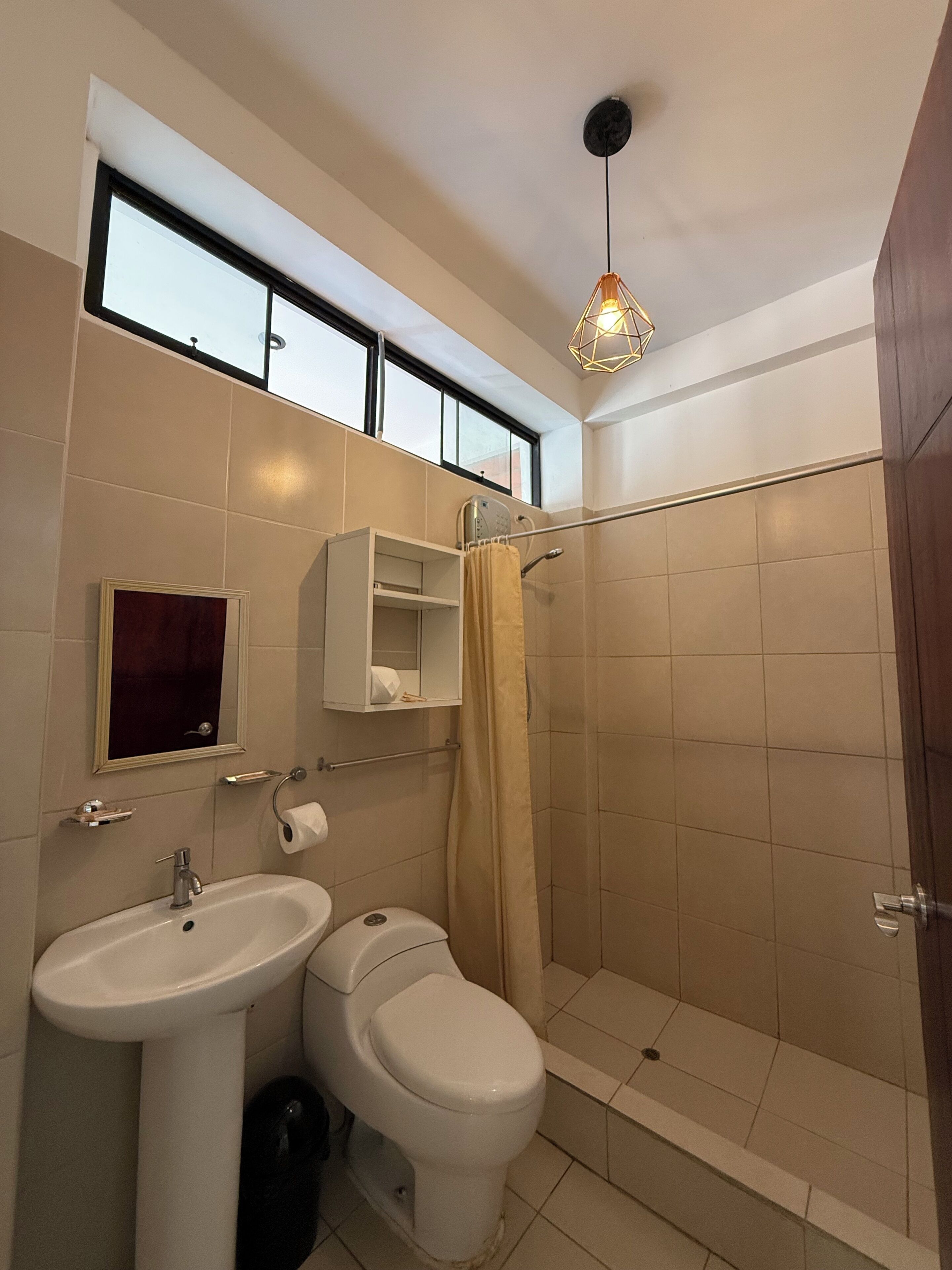 A bathroom with a sink, toilet, shower, and a window above the sink.