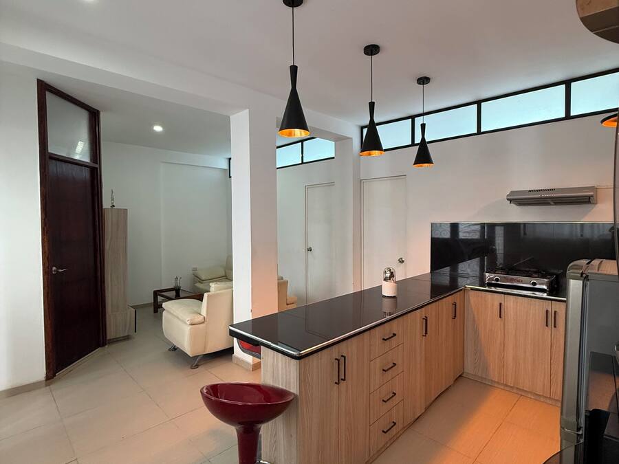 A modern kitchen with a central island, pendant lights, and a refrigerator.