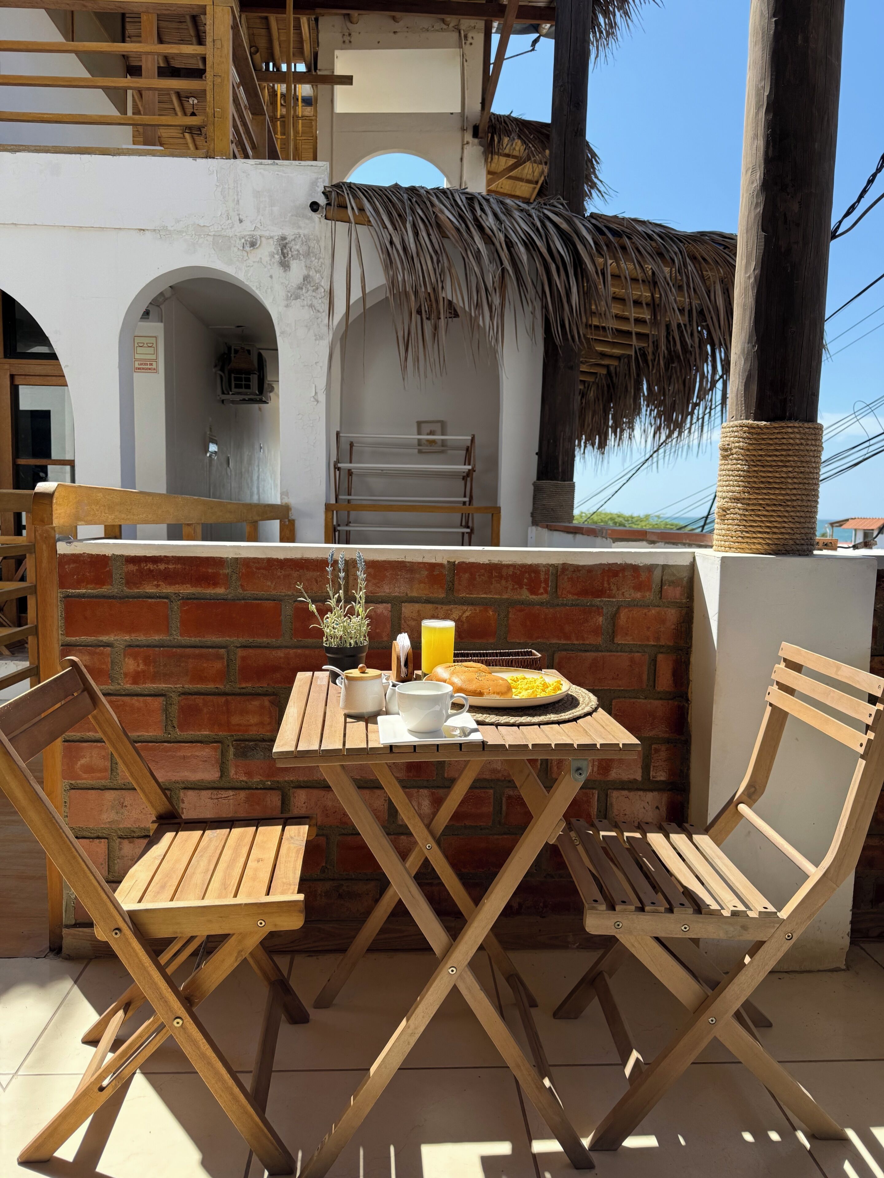 Un área de comedor al aire libre con pared de ladrillo, muebles de madera y estructura de techo de paja.