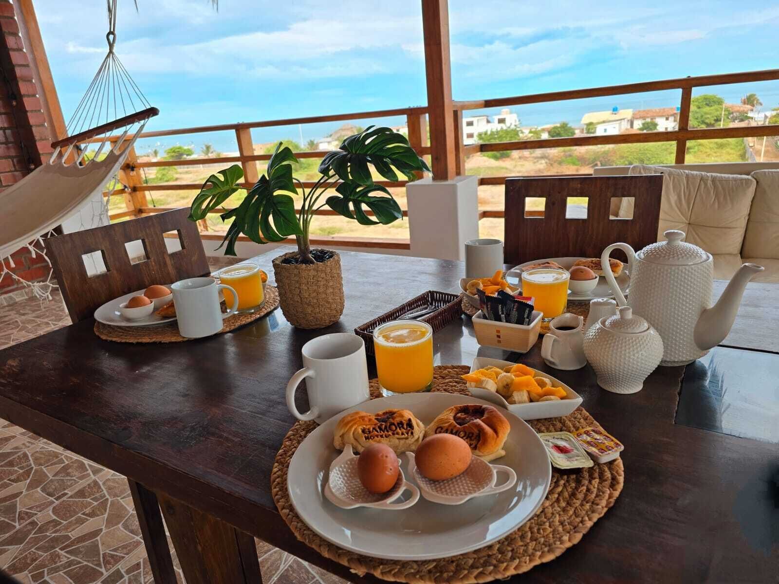 A breakfast setup with a table, chairs, a hammock, and a view of the sea.