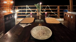 A dining area with a wooden ceiling, brick walls, and a thatched roof. There are two tables with woven placemats, candles, and a decorative glass centerpiece. - Gamora Hotel Playa (Los Organos)