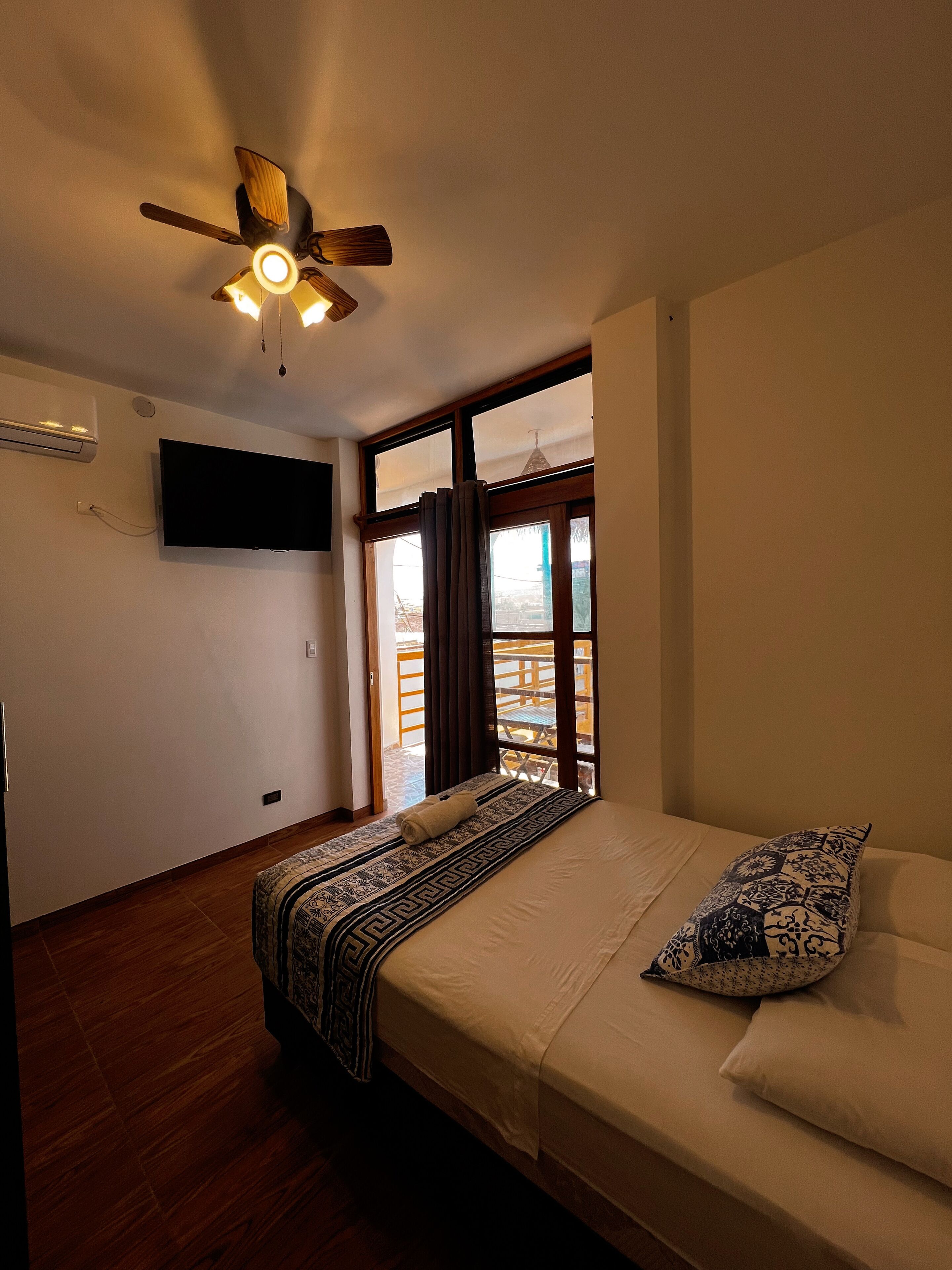 A bedroom with a bed, a ceiling fan, a TV, and a window with curtains.
