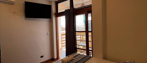 A bedroom with a bed, a ceiling fan, a TV, and a window with curtains.