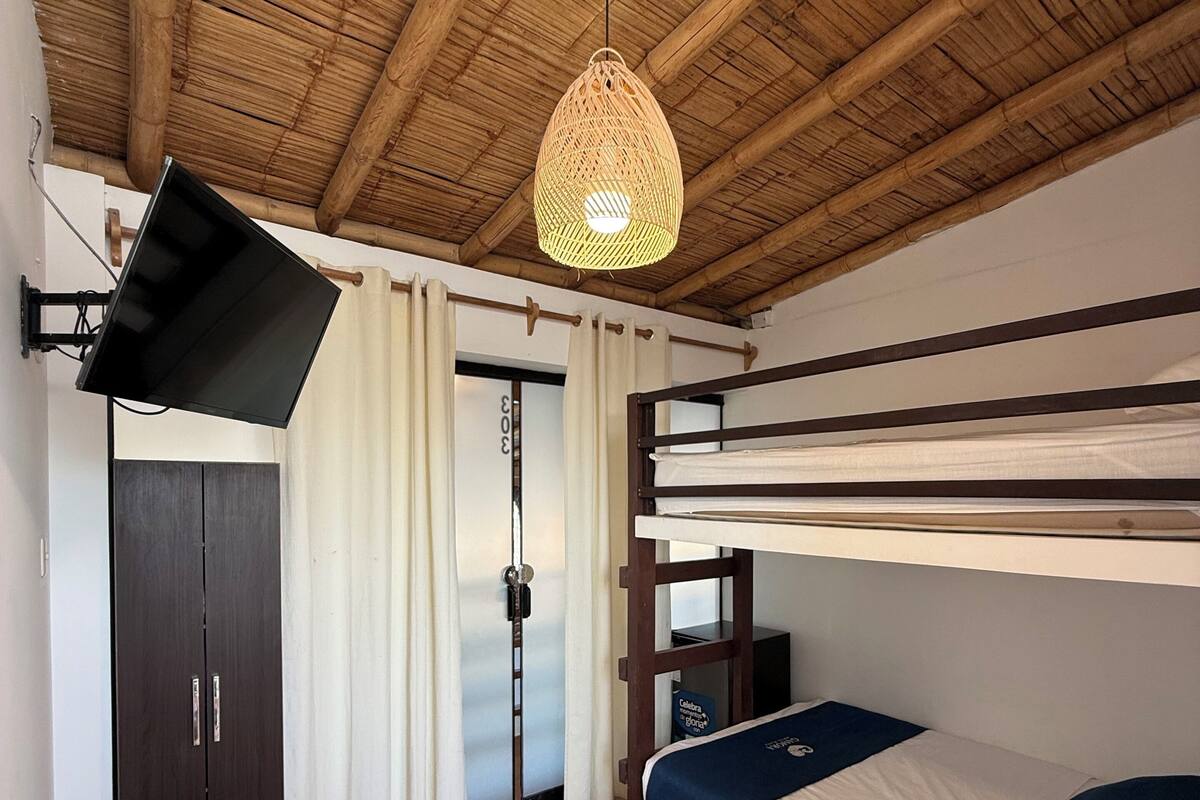 Un letto a castello con televisore montato sulla parete, un tavolo di legno e un lampadario intrecciato al soffitto.
