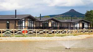A row of modern cabins with large windows, a wooden fence, and a mountain in the background. - Stan Hollis Lodge - UKC4063 (Great Ayton, near Stokesley)