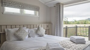A neatly made bed with patterned pillows and a folded towel, a window with a patterned valance, and a view of a balcony with a railing. - Stan Hollis Lodge - UKC4063 (Great Ayton, near Stokesley)