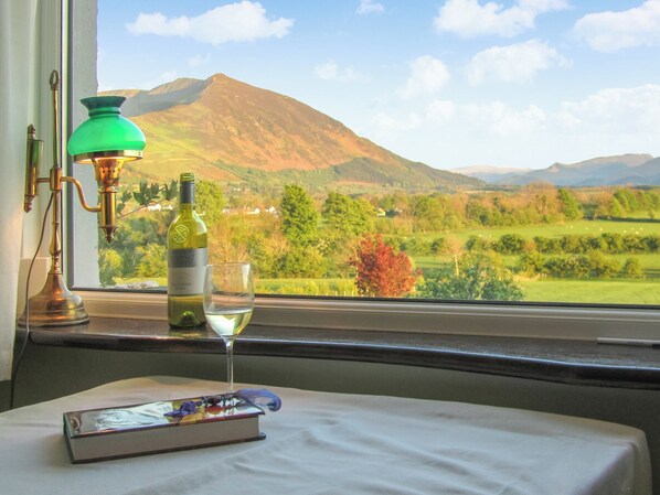 A table with a bottle of wine, a glass, and a book, with a view of a mountainous landscape through a window.