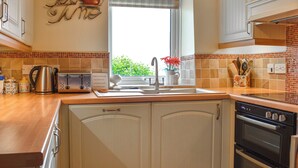 A kitchen with white cabinets, a stainless steel kettle, a toaster, and a window with a view of greenery. - 2 bedroom accommodation in Bassenthwaite, near Keswick (Bassenthwaite, near Keswick)