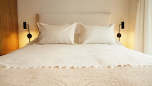 A neatly made bed with a textured white duvet, two pillows, and two wall-mounted bedside lamps. - Hestia at Paraguay 4700 (Buenos Aires)