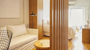 A modern hotel room with a sofa, a small round table with a candle, a bed, and a wooden partition. - Hestia at Paraguay 4700 (Buenos Aires)
