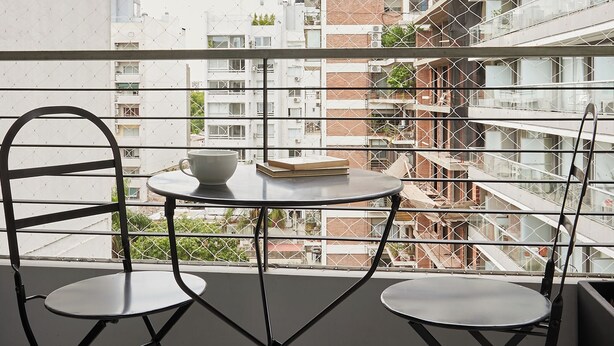 A balcony with two chairs and a table, overlooking a cityscape with multiple buildings. - Hestia at Paraguay 4700 (Buenos Aires)