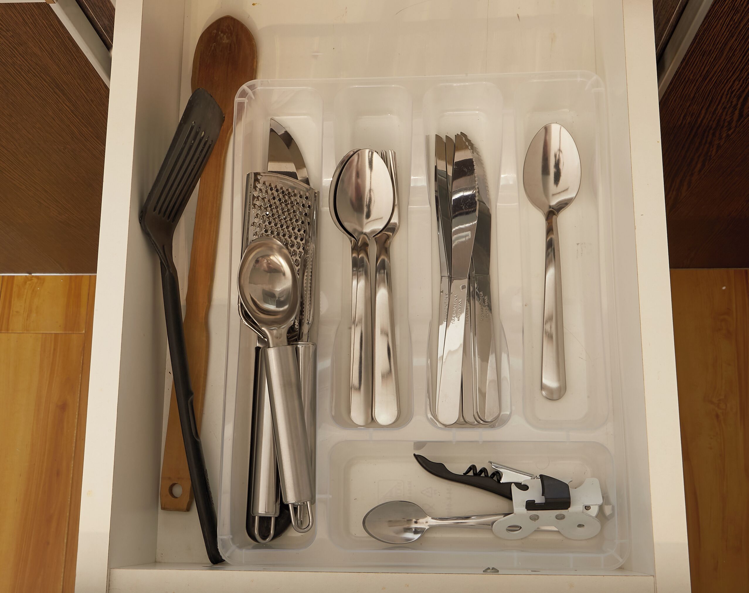 A drawer containing various kitchen utensils including a grater, spoons, a knife, and a spatula.