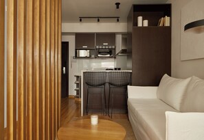 A modern kitchen with a microwave, toaster, and oven. There is a wooden dining table with two chairs and a white sofa in the living area. - Hestia at Paraguay 4700 (Buenos Aires)