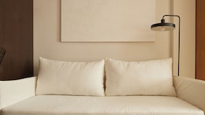 A beige sofa with two cushions, a black floor lamp, and a plain wall with a textured pattern. - Hestia at Paraguay 4700 (Buenos Aires)