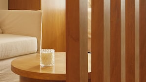 A wooden partition with a glass of water on a round table in a room with a white sofa. - Hestia at Paraguay 4700 (Buenos Aires)