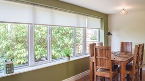 A dining area with a table and chairs, a window with blinds, and a hanging light fixture. - 2 bedroom accommodation in Ardrossan, near Ayr (Ardrossan, near Ayr)