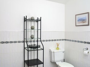 Kylpyhuone, jossa on wc, lasihylly koriste-esineitä varten ja seinällä kehystetty taulu.