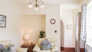 A living room with two sofas, a side table with a lamp, a clock, and a plant. - 2 bedroom accommodation in Ardrossan, near Ayr (Ardrossan, near Ayr)