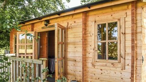 Una cabaña de madera con terraza, una puerta de entrada y una ventana.
