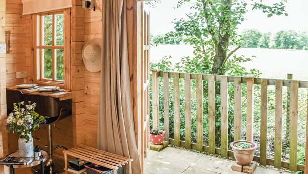 Una cabaña de madera acogedora con comedor, una ventana con cortinas y vistas a un jardín y un lago.