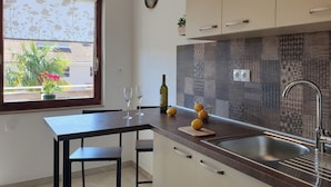 A modern kitchen with a dark countertop, white cabinets, and a patterned backsplash. There are two wine glasses and a bottle on the counter. - Apartment with balcony, parking near the center and the sea (Crikvenica)