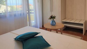 A bedroom with a bed, two pillows, a small table with a vase, and a bench. - Apartment with balcony, parking near the center and the sea (Crikvenica)