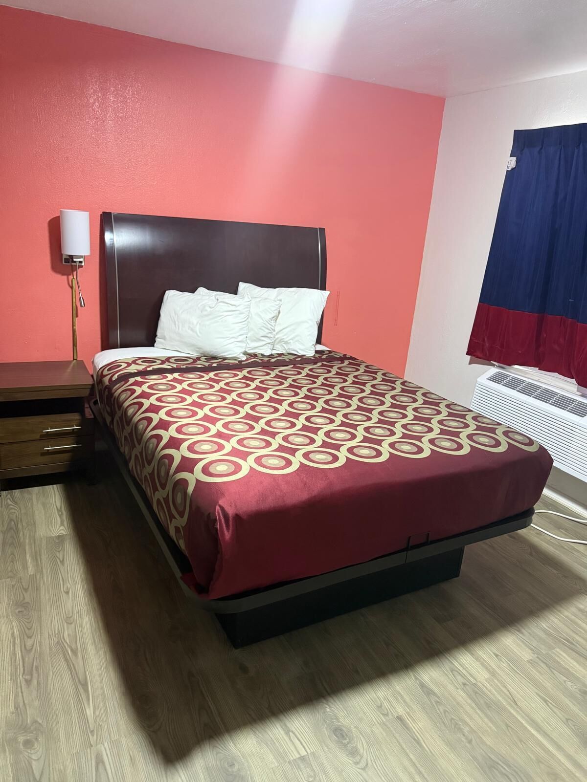 Una habitació d'hotel amb un llit, una tauleta de nit, una làmpada i una finestra amb cortines.