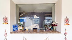 Un espace d’accueil d’hôtel avec un panneau indiquant que le petit-déjeuner est servi, un appareil photo sur un trépied et des éléments de décoration, notamment un vase avec des fleurs et une petite statue.