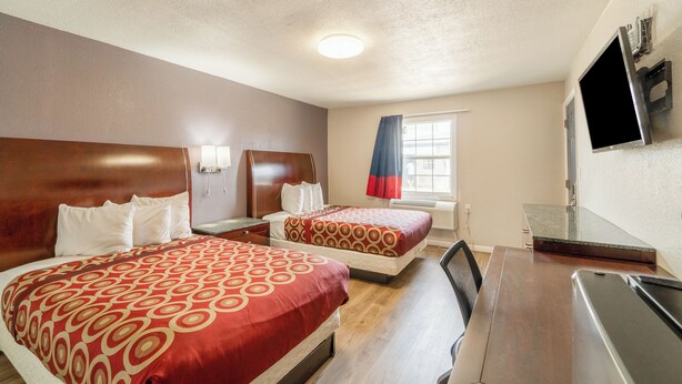 Une chambre d’hôtel avec deux lits, un bureau, une télévision et une fenêtre avec des rideaux.