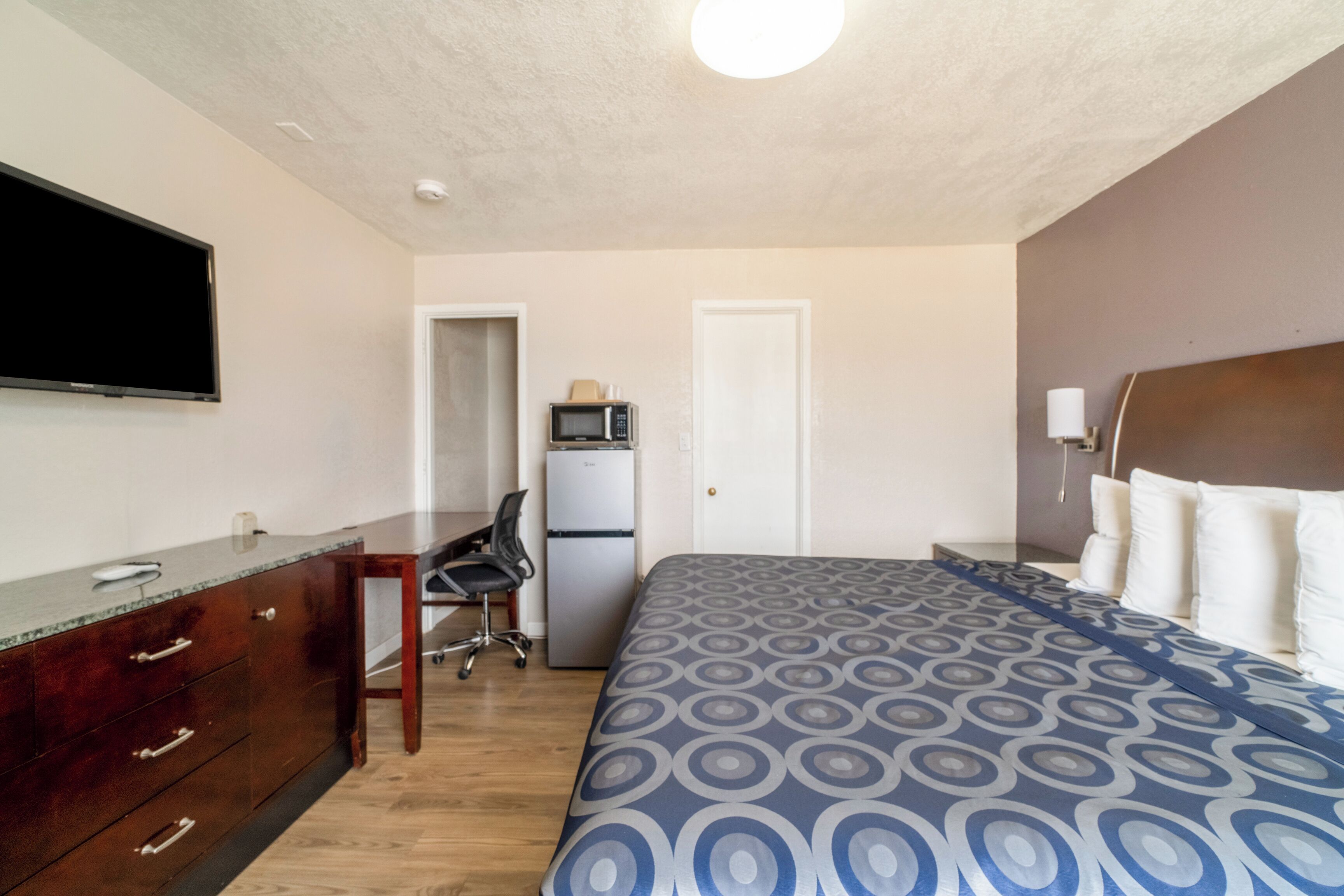 A hotel room with a bed, a desk, a chair, a television, a microwave, and a refrigerator.