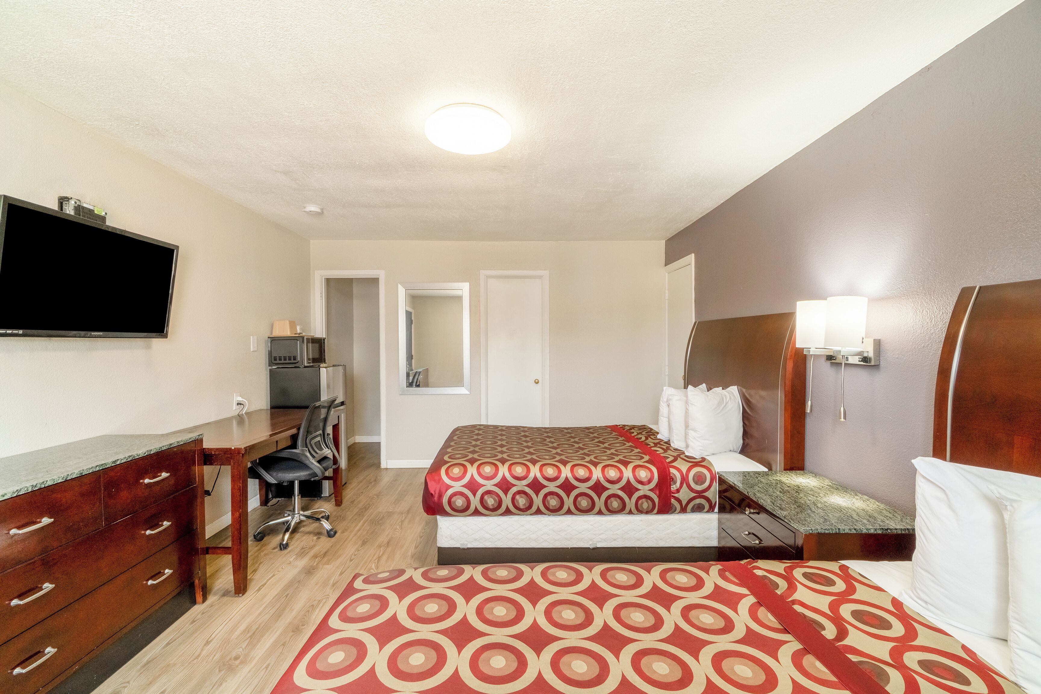 A hotel room with two beds, a desk, a TV, and a bathroom visible through an open door.
