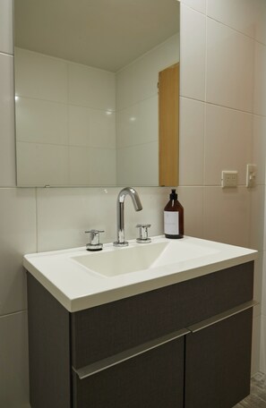 A bathroom with a white sink, two faucets, a mirror, and a bottle of soap. - Hestia at Cabrera 3200 (Buenos Aires)