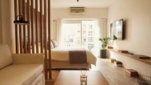 A modern hotel room with a bed, a sofa, a coffee table, a TV, and a balcony with a view of buildings. - Hestia at Cabrera 3200 (Buenos Aires)