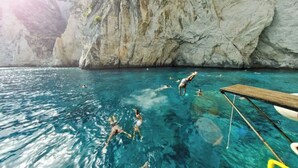 Klares blaues Meer mit badenden Menschen und einer hölzernen Anlegestelle, die ins Wasser ragt.