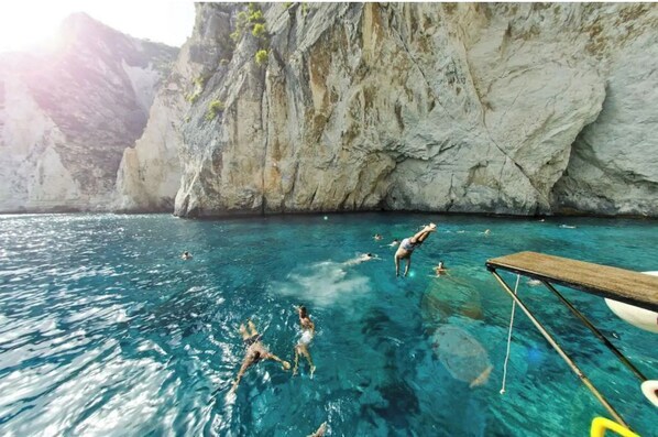 A clear blue sea with people swimming and a wooden dock extending into the water.
