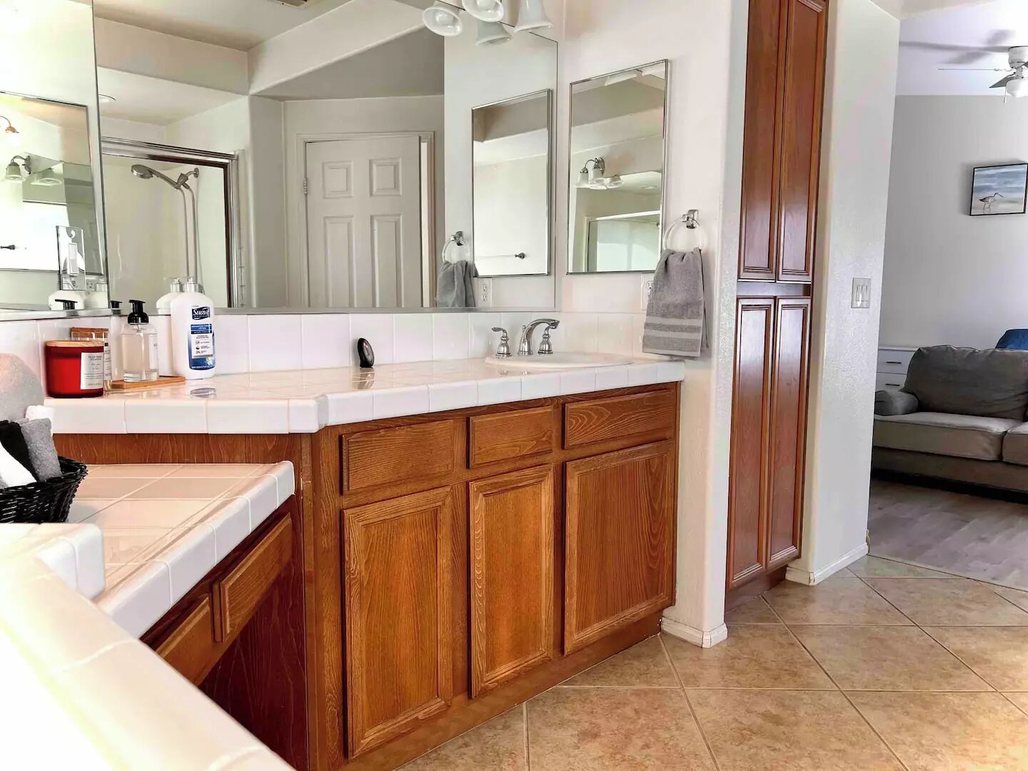 A bathroom with a large mirror, wooden cabinets, a sink, and a shower.