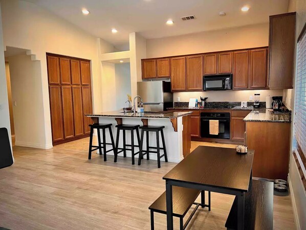 A modern kitchen with wooden cabinets, a central island with stools, a built-in oven, and a microwave.