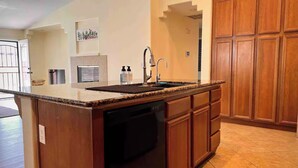 Una cucina con piano di lavoro in granito, mobili in legno, lavastoviglie e lavello.