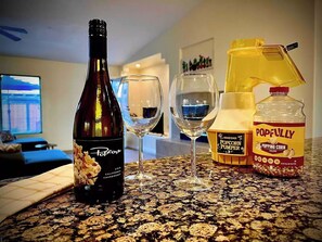 A bottle of Popcorn Chardonnay, two wine glasses, a popcorn popper, and a bottle of Popfully popping corn on a kitchen counter.
