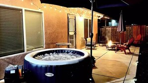 Un'area patio all'aperto con vasca idromassaggio, posti a sedere e luci decorative.