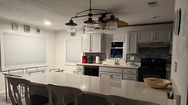 A modern kitchen with white cabinetry, a central island with bar stools, a built-in oven, and a ceiling fan. - Beautiful Beach House In Fort Morgan !  (Gulf Shores)